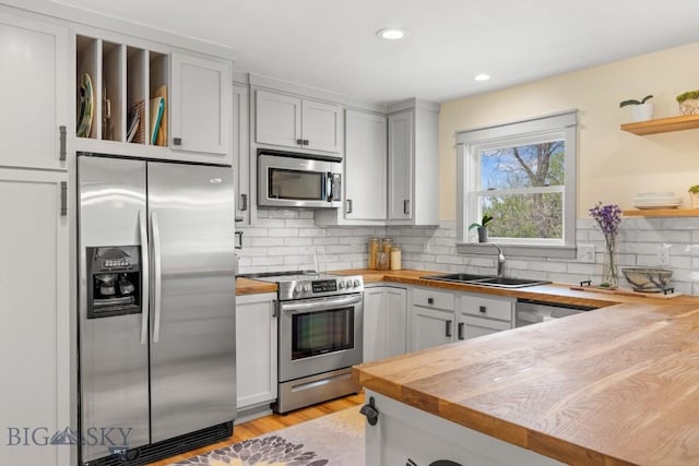 kitchen featuring stainless steel appliances, butcher block counters, open shelves, a sink, and recessed lighting