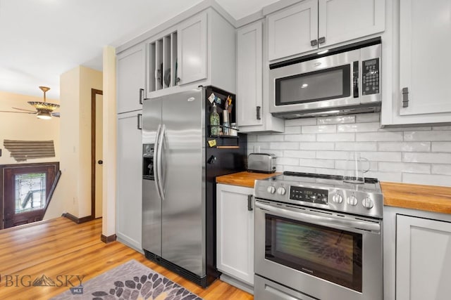 kitchen featuring appliances with stainless steel finishes, butcher block counters, backsplash, light wood finished floors, and ceiling fan