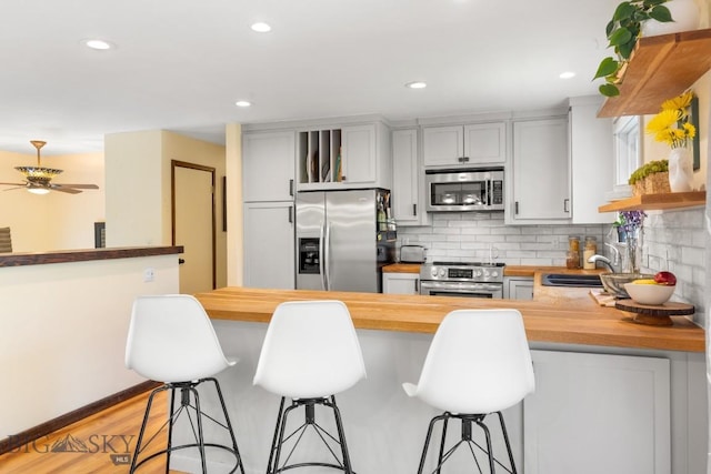 kitchen with stainless steel appliances, butcher block countertops, a sink, backsplash, and a peninsula