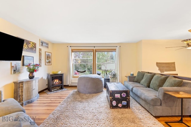 living room with light wood-style floors, a wood stove, and a ceiling fan