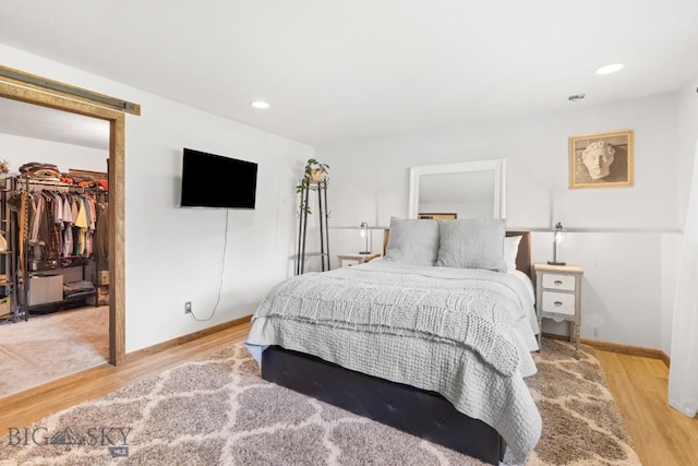 bedroom featuring a walk in closet, light wood-style flooring, baseboards, a closet, and recessed lighting