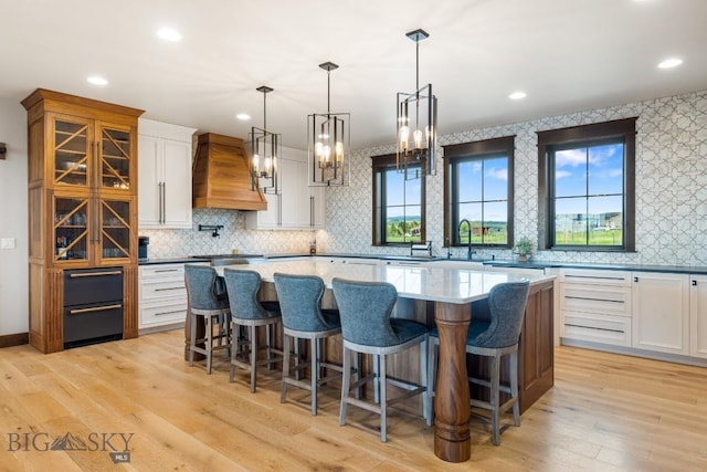 200 Miller Point Pl, Belgrade, MT 59714 - kitchen with premium range hood, light wood-style floors, white cabinetry, backsplash, and a spacious island
