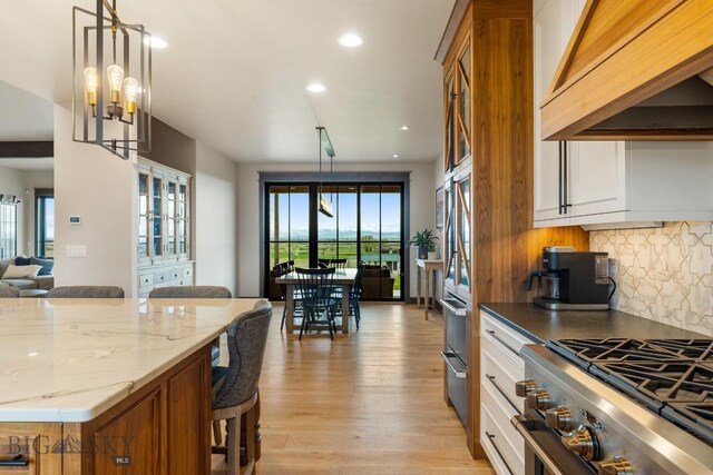200 Miller Point Pl, Belgrade, MT 59714 - kitchen featuring stainless steel stove, custom exhaust hood, a kitchen breakfast bar, light wood-type flooring, and decorative backsplash
