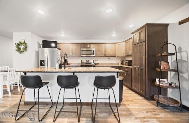 705 Halfpipe St Unit B, Belgrade, MT 59714 - kitchen with stainless steel appliances, a sink, light wood-style flooring, an island with sink, and a breakfast bar area
