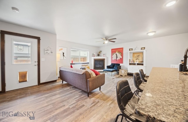 705 Halfpipe St Unit B, Belgrade, MT 59714 - living room featuring a ceiling fan, light wood-type flooring, a glass covered fireplace, and baseboards