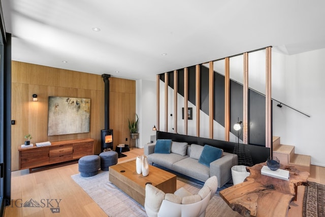 living area with a wood stove, stairs, light wood-style flooring, wooden walls, and recessed lighting