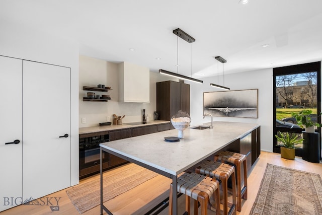 kitchen with black oven, light wood finished floors, a sink, modern cabinets, and an island with sink