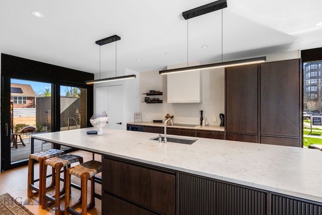 kitchen featuring a sink, dark brown cabinetry, light wood finished floors, hanging light fixtures, and recessed lighting