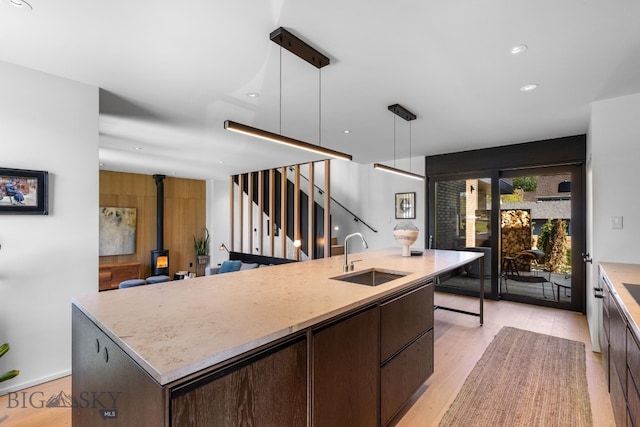 kitchen with a sink, dark brown cabinetry, a wood stove, a center island with sink, and recessed lighting