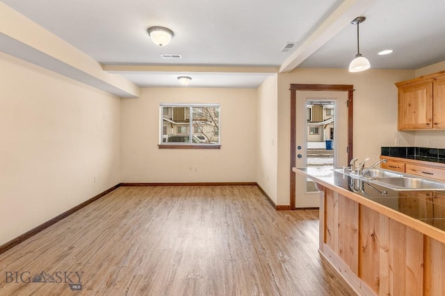 unfurnished dining area with a sink, light wood-type flooring, baseboards, and beam ceiling