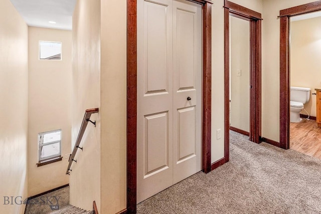 hallway featuring an upstairs landing, light colored carpet, and baseboards