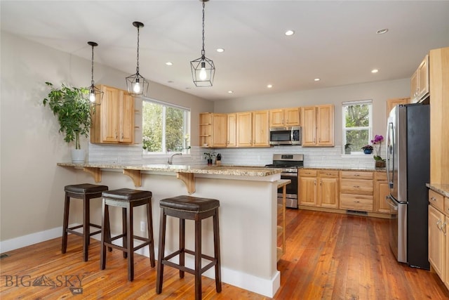 508 Coral Dr, Belgrade, MT 59714 - kitchen with stainless steel appliances, light brown cabinetry, decorative backsplash, a kitchen bar, and light stone counters