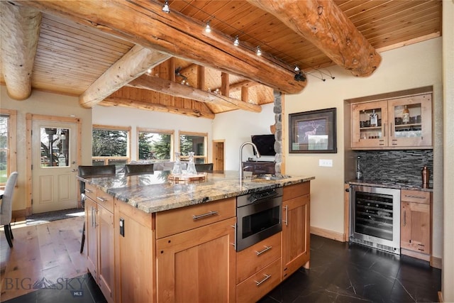 9704 River Rd, Bozeman, MT 59718 - kitchen featuring beverage cooler, wooden ceiling, beamed ceiling, light stone countertops, and an island with sink