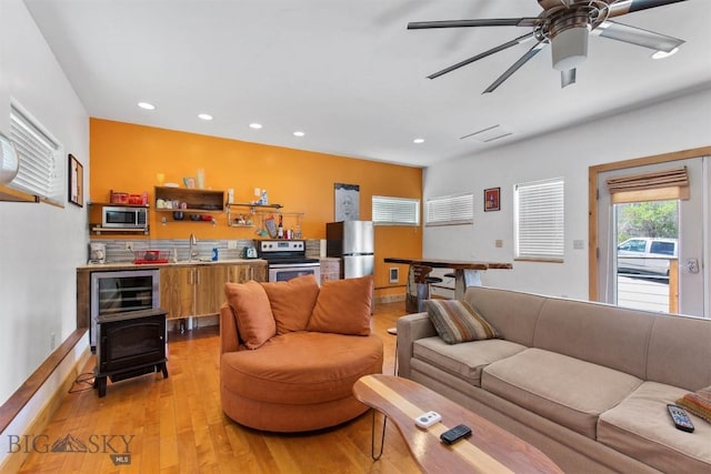 living area featuring recessed lighting, light wood finished floors, ceiling fan, and a wood stove