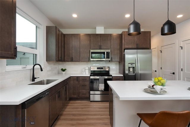 kitchen featuring stainless steel appliances, a sink, light wood-style flooring, tasteful backsplash, and dark brown cabinetry