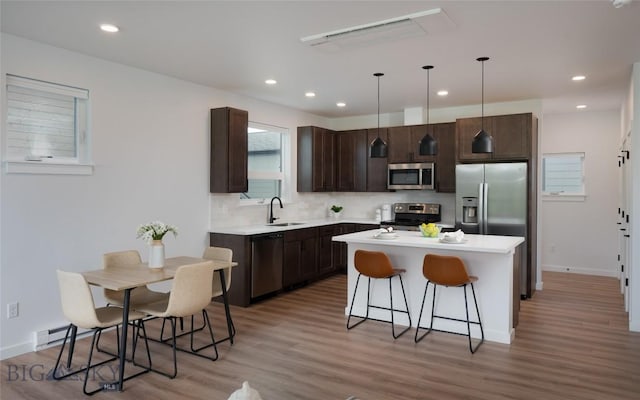 kitchen with stainless steel appliances, dark brown cabinets, a sink, light countertops, and light wood-style flooring