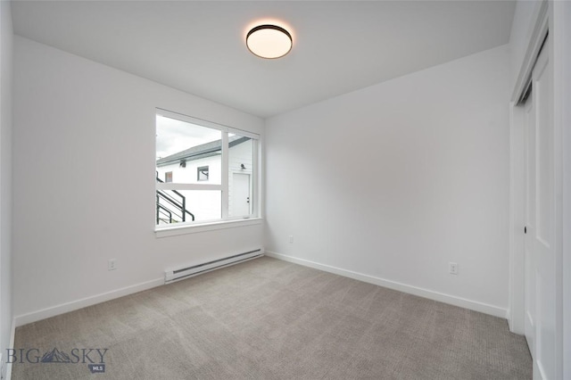spare room with baseboard heating, light carpet, and baseboards