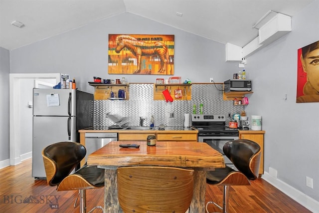 kitchen with appliances with stainless steel finishes, wood finished floors, lofted ceiling, backsplash, and baseboards