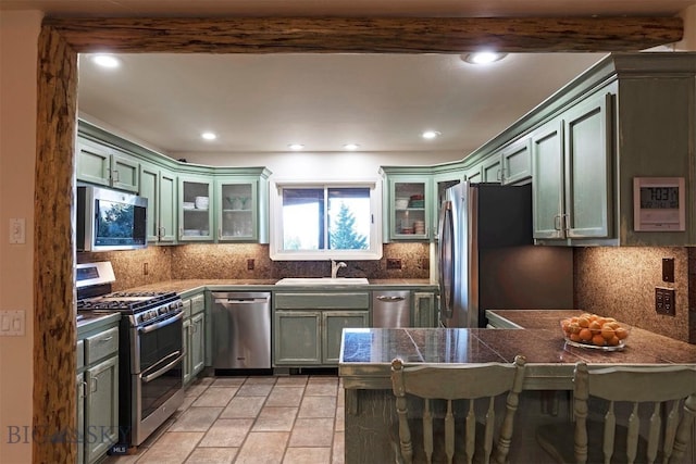 kitchen featuring stainless steel appliances, a sink, green cabinets, backsplash, and a peninsula