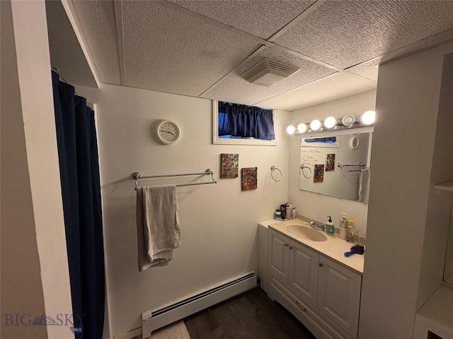 full bath with a baseboard radiator, a drop ceiling, vanity, and wood finished floors