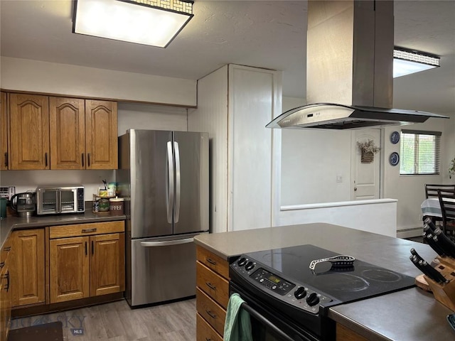 kitchen with island range hood, electric range oven, freestanding refrigerator, brown cabinets, and light wood-type flooring