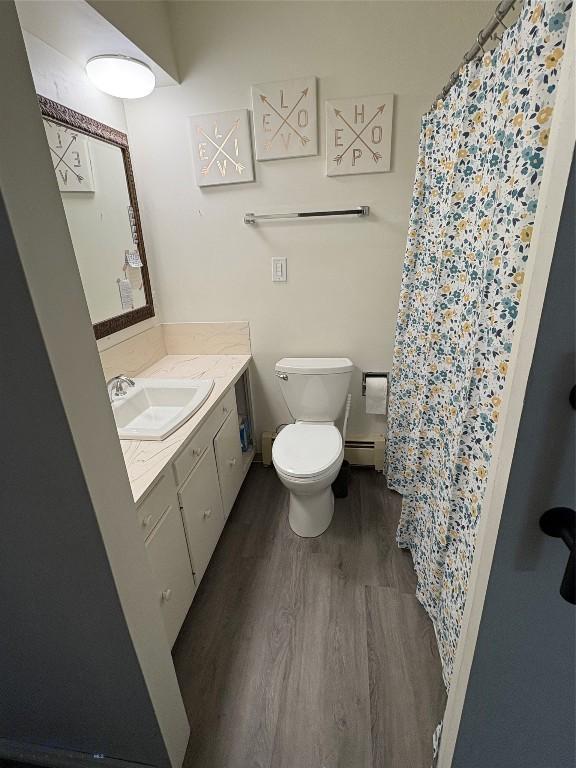 bathroom with wood finished floors, toilet, vanity, baseboard heating, and curtained shower