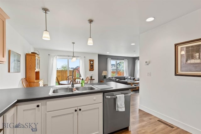 kitchen featuring stainless steel dishwasher, a sink, open floor plan, light wood-style flooring, and pendant lighting