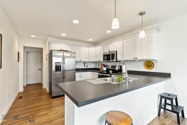 kitchen featuring stainless steel appliances, dark countertops, a peninsula, white cabinetry, and recessed lighting