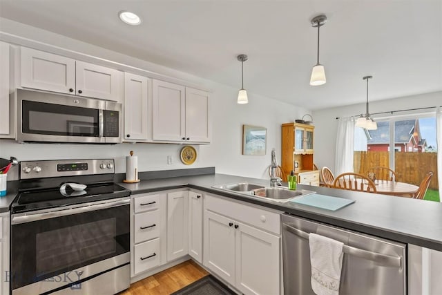 kitchen with stainless steel appliances, a sink, white cabinets, a peninsula, and dark countertops