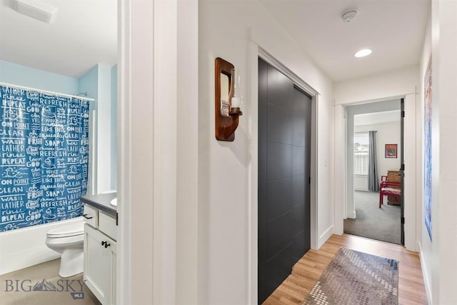 hall featuring light wood-style flooring, baseboards, and recessed lighting