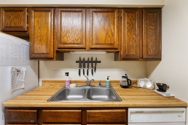 kitchen featuring a sink, dishwasher, light countertops, and brown cabinetry