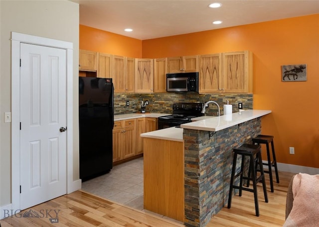 128 Droulliard Ave, Bozeman, MT 59718 - kitchen with black appliances, a peninsula, a breakfast bar area, tasteful backsplash, and light countertops