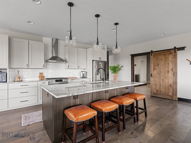 449 Minni Hall Rd, Bozeman, MT 59715 - kitchen featuring wall chimney exhaust hood, appliances with stainless steel finishes, a barn door, backsplash, and dark wood-style flooring