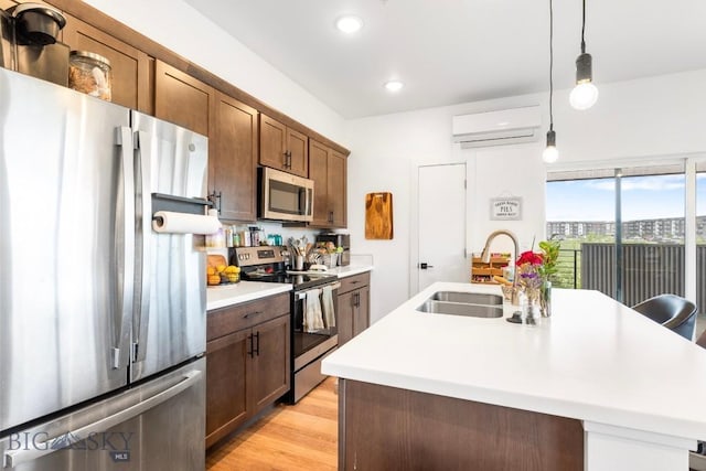 kitchen with appliances with stainless steel finishes, a sink, light countertops, a kitchen island with sink, and light wood-type flooring