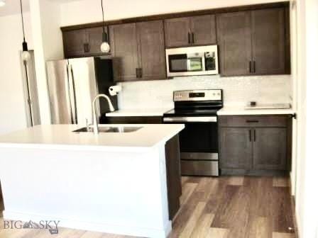 kitchen featuring appliances with stainless steel finishes, a sink, light countertops, dark wood-style flooring, and dark brown cabinets