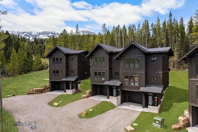 back of property featuring an attached garage, driveway, a wooded view, and a lawn