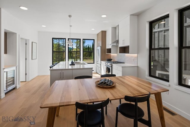 dining space with baseboards, light wood-style floors, wine cooler, and recessed lighting