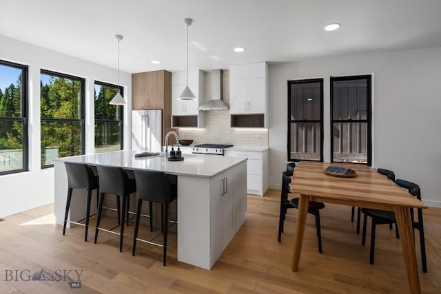 kitchen with wall chimney exhaust hood, modern cabinets, decorative backsplash, refrigerator, and light countertops