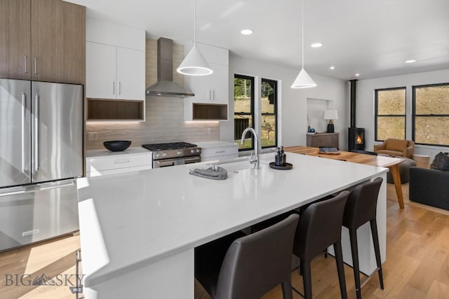 kitchen with appliances with stainless steel finishes, wall chimney exhaust hood, a wood stove, light countertops, and white cabinets