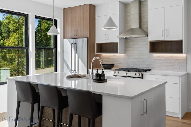 kitchen with wall chimney exhaust hood, stainless steel fridge, range, and modern cabinets