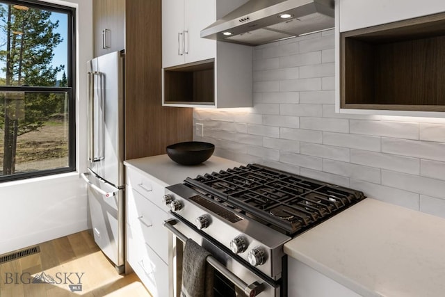 kitchen featuring wall chimney range hood, appliances with stainless steel finishes, open shelves, and light countertops