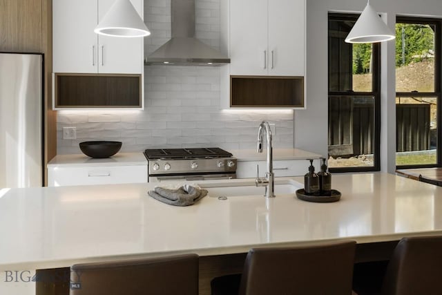 kitchen with wall chimney exhaust hood, stainless steel gas range, light countertops, white cabinetry, and backsplash