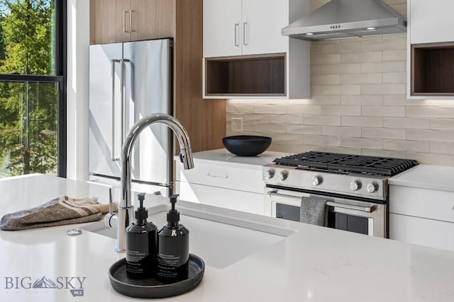kitchen with wall chimney exhaust hood, stainless steel gas stove, light countertops, and tasteful backsplash