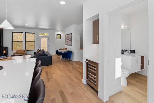 living room with wine cooler, light wood finished floors, recessed lighting, baseboards, and a wood stove