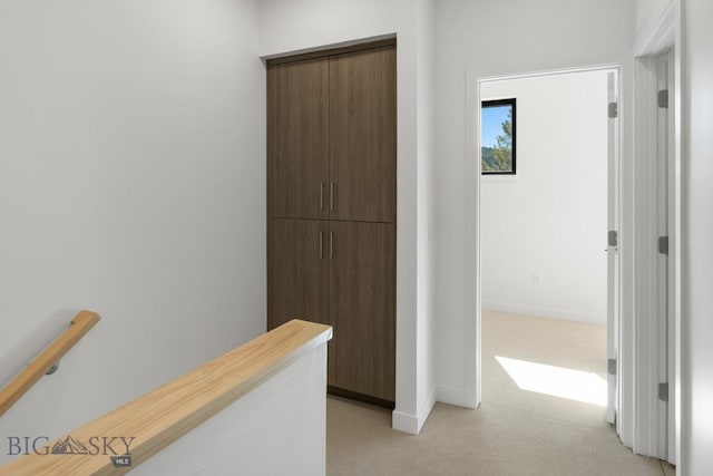 hallway with an upstairs landing, light colored carpet, and baseboards