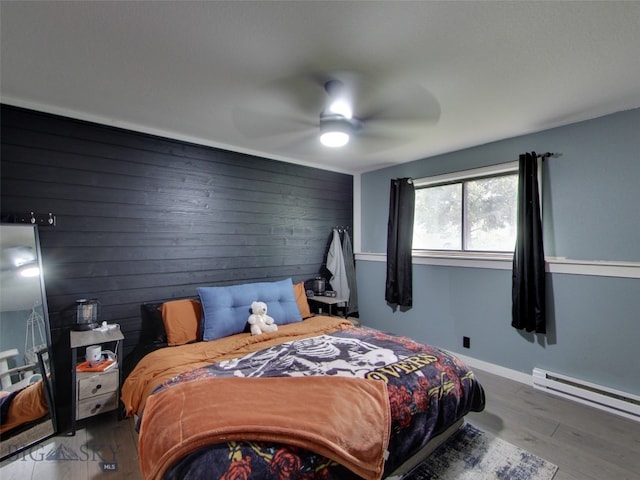 902 E Gallatin Ave, Belgrade, MT 59714 - bedroom with baseboard heating, wood finished floors, wooden walls, a ceiling fan, and baseboards