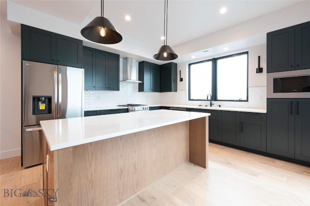 kitchen with stainless steel refrigerator with ice dispenser, wall chimney range hood, a sink, a center island, and light wood-style flooring
