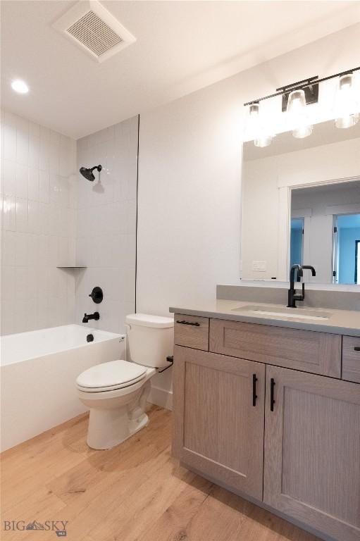 bathroom with wood finished floors, toilet, vanity, and shower / bathtub combination