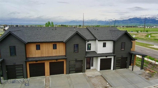 view of property featuring an attached garage, a mountain view, driveway, and roof with shingles