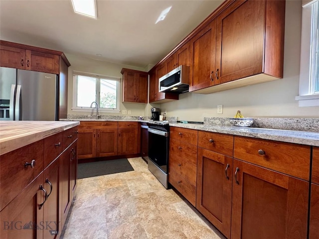 205 E Chinook St, Livingston, MT 59047 - kitchen featuring stainless steel appliances, brown cabinetry, wooden counters, and stone finish flooring